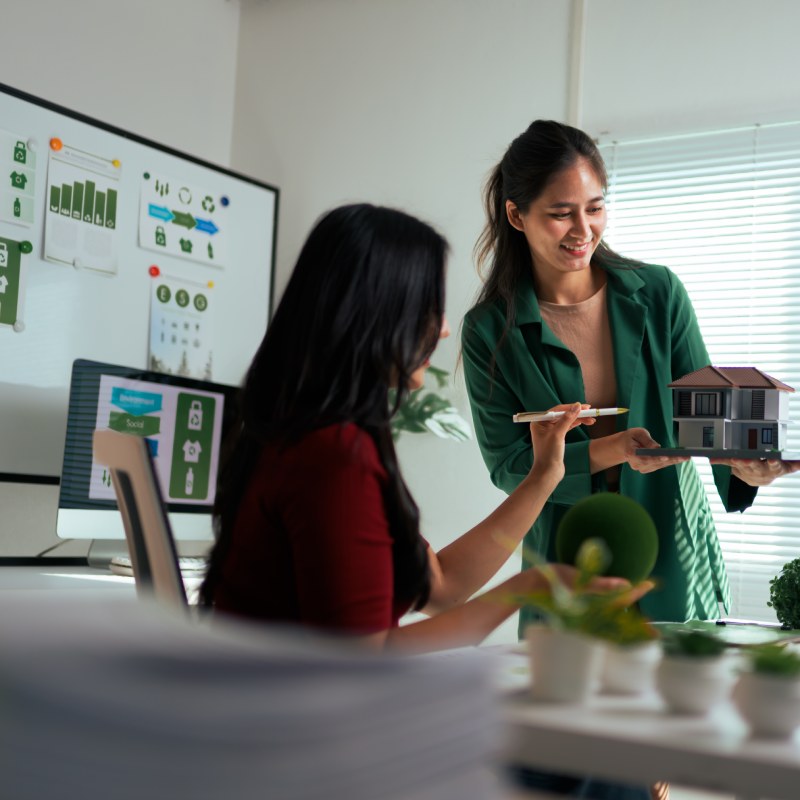 Architect women discussing a sustainable home model and charts in an office meeting